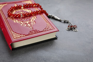 Muslim prayer beads and Quran on grey stone table, closeup