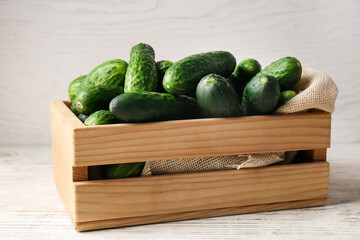 Crate full of fresh ripe cucumbers on white wooden table