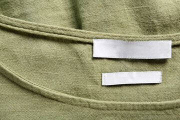 Blank clothing label on green apparel, top view. Space for text