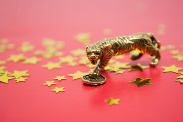 Bronze figure of a tiger with coin on a red background with golden stars, copy space. Wishes of...