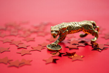 Bronze figure of a tiger with coin on a red background with red stars, copy space. Wishes of good...