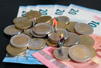 Miniature figurines of worker working on a pile of money