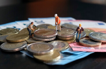 Obraz premium Miniature figurines of worker working on a pile of money