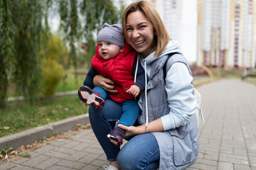 portrait of a young mother woman with her one-year-old child in her arms against the backdrop of a city park