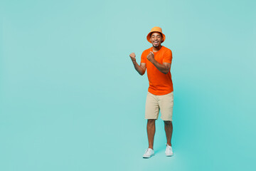 Fototapeta na wymiar Full body happy young man of African American ethnicity 20s wear orange t-shirt hat doing winner gesture celebrate say yes isolated on plain pastel light blue cyan background People lifestyle concept