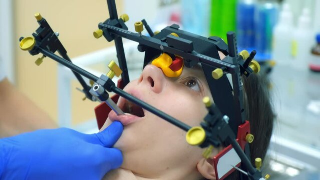 Orthodontology treatment and cure concept. Orthodontist is fixing equipment on woman's patient teeth preparing to condylography. Examination and treatment of mandibular joints. Dentistry and clinic.