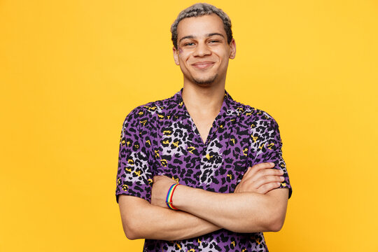 Young cheerful happy fun gay man wearing purple animal print shirt hold hands crossed folded look camera isolated on bright plain yellow color background studio portrait Lifestyle lgbtq pride concept