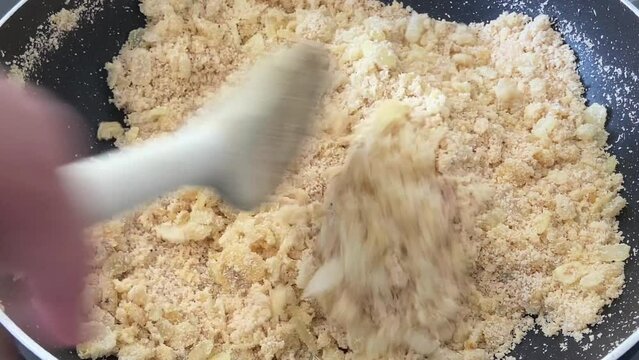 Preparing farofa (Brazilian toasted cassava flour) toasting in a pan on the electric stove. Adding the cassava flour and stirring continuously with a wooden spoon.