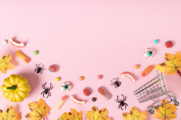 Halloween party background with pumpkins, candy and supermarket basket on pink background. Space...