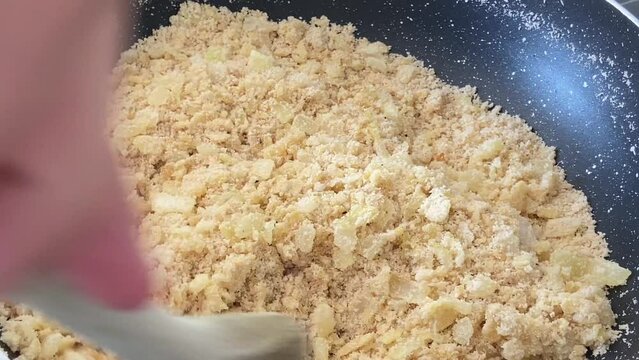 Preparing farofa (Brazilian toasted cassava flour) toasting in a pan on the electric stove. Adding the cassava flour and stirring continuously with a wooden spoon.