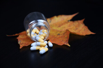 Pills and autumn maple leaf on dark wooden table, bottle with scattered capsules. Pharmacy, antidepressants, vitamins for immunity in flu season