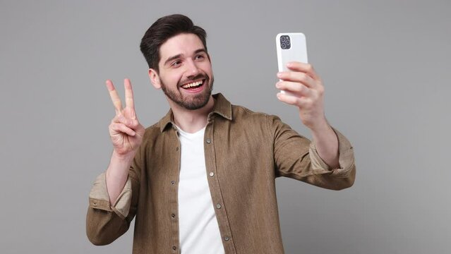 Young cheerful fun happy caucasian man 20s he wear brown shirt doing selfie shot on mobile phone post photo on social network isolated on plain grey background studio portrait People lifestyle concept