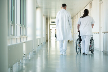 Doctor and nurse pushing wheelchair with woman patient in hospital