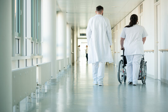 Doctor and nurse pushing wheelchair with woman patient in hospital