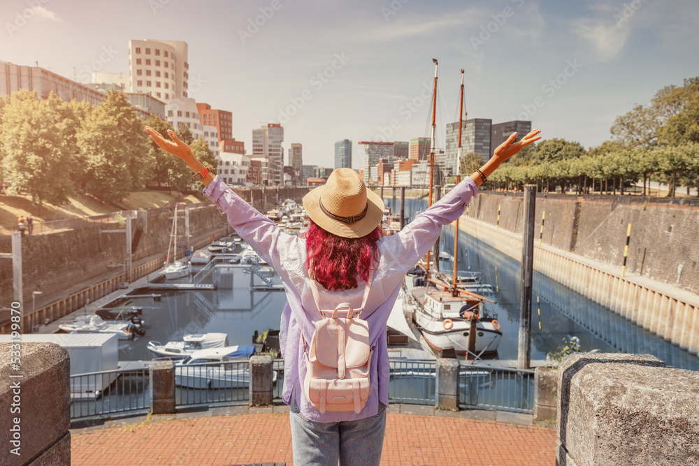 Wall mural A girl traveler enjoys a beautiful view in the Media Bay harbor and marina with parked boats and yachts during a tourist trip or a student education in Dusseldorf, Germany - Wall murals