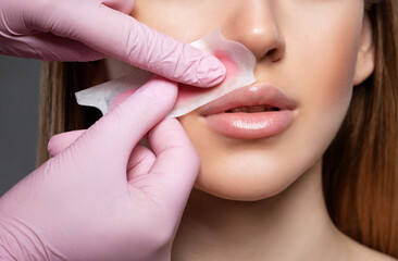 The beautician makes a mustache removal with wax in a young woman. hair removal procedure on a...