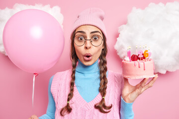 Horizontal shot of shocked woman with pony tails stares with omg expression holds cake with burning...
