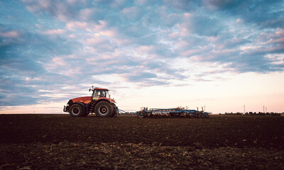 Fototapeta premium Tractor on field tilling the soil during sunset