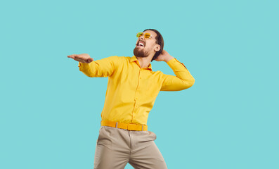 Time for party. Cheerful positive and energetic man with funny crazy expression having fun on light blue background. Millennial hipster man in trendy glasses and yellow shirt having fun and dancing.