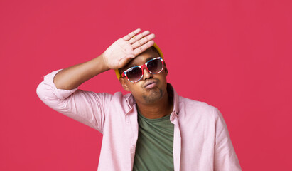 Touching his forehead young african american man in UK, Britain flag sunglasses, wearing casual looks tired or exhausted facial expression, dodged a bullet, in yellow hat isolated on red background - obrazy, fototapety, plakaty
