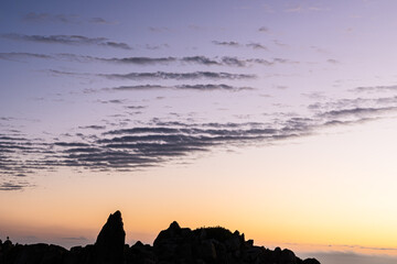 dawn sky with ridged cloud pattern and coastal rock formations silhouetted against sky and ocean bay waters - 533202862