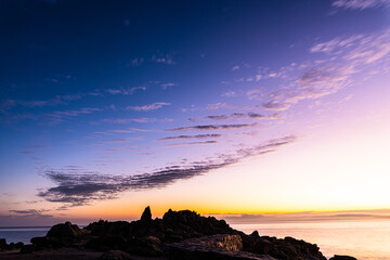 dawn sky with ridged cloud pattern and coastal rock formations silhouetted against sky and ocean bay waters - 533202877