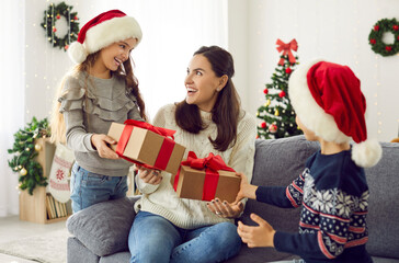 Obraz na płótnie Canvas Happy joyful young mother gets unexpected presents from her loving children on Xmas Day. Woman with pleasantly surprised face receives greetings from her young son and daughter on Christmas morning.