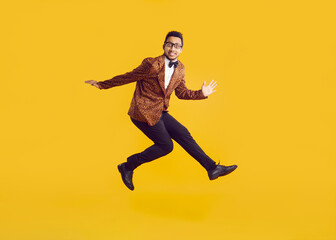 Fototapeta na wymiar Cheerful funny dark-skinned young man in leopard jacket having fun jumping on yellow background. Portrait of jumping stylish, fashionable and eccentric guy with funny expression. Banner. Full length.