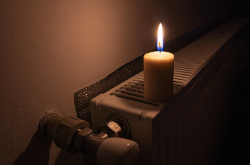Burning candle on the radiator heating in dark home. Shutdown of heating and electricity, power...