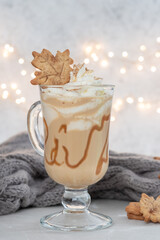 Pumpkin spice latte in a glass mug with caramel and cinnamon cookies with Autumn decoration