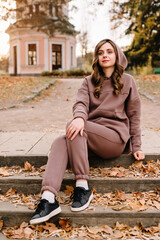 Young woman in hoodie sitting on the steps in an autumn park. Sunny weather. Fall season.