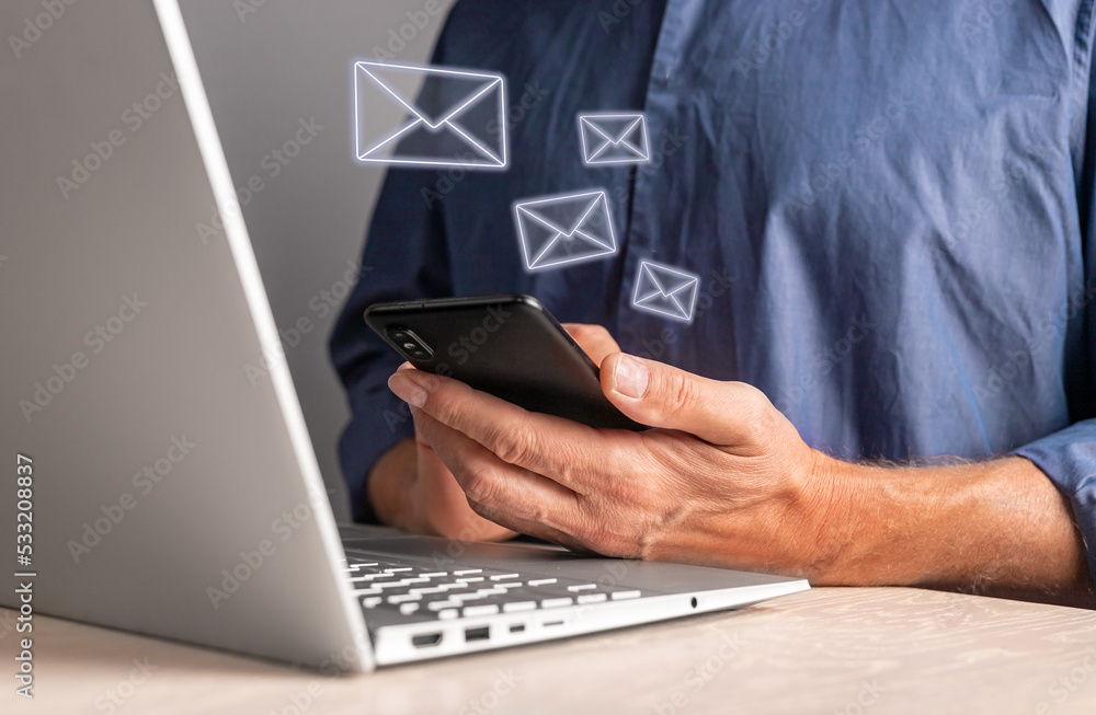 Poster Man using phone for receiving or sending messages while working on laptop. Male sitting at table with computer and holding smartphone. E-mail flow. High quality photo