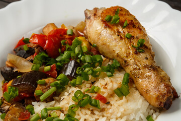 Rice with stewed vegetables in sauce and chicken leg in a white plate close-up.