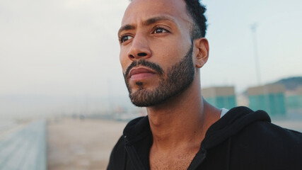 Close-up, young bearded male athlete standing on the embankment, looking at the sea.