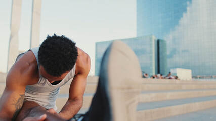 Close up, young bearded male athlete doing warm-up, stretching legs before training while standing on the embankment