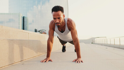 Young bearded male athlete doing workout, push ups on the embankment