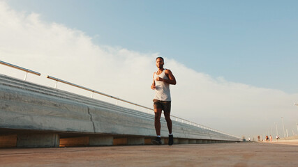 Young bearded male fit athlete runs along the promenade