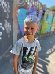  cute funny boy with bright blue colored hair on a background of a colored wall with graffiti