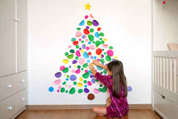 The girl decorates the wall in the nursery with paper multicolored circles that make up the shape...