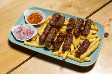 Kebabs served on a wooden board with french fries and onion