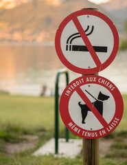 no dogs sign and no smoking sign in a public park with a lake in the background