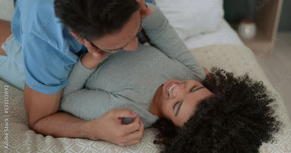 Wall mural Happy, couple and love in bedroom smile, fun and playful laughter and affection together at home. Man and woman playing on a bed smiling in joyful happiness, relaxing and bonding in a relationship