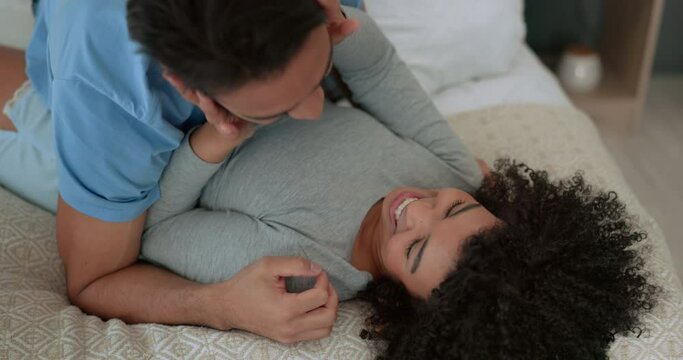 Happy, couple and love in bedroom smile, fun and playful laughter and affection together at home. Man and woman playing on a bed smiling in joyful happiness, relaxing and bonding in a relationship