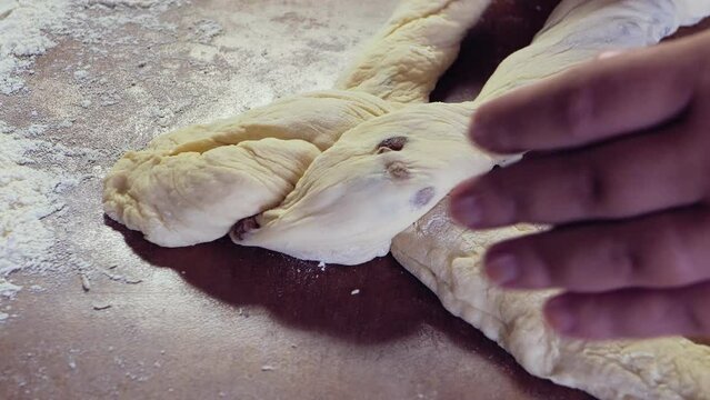 The hands of a Jewish woman weave challah dough with a pigtail for Shabbat with raisins