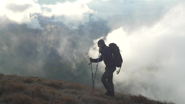 A man while hiking in the mountains shrouded in clouds. A man walks above the sky in a beautiful mountain landscape. The boy is traveling with a backpack. The concept of freedom and beauty. 