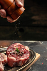 chef pours pepper on raw steak. Backstage of preparing grilled pork meat. Culinary, cooking concept. vertical image. place for text