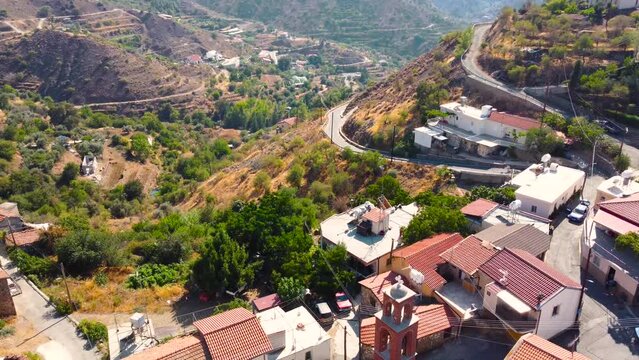 Aerial drone footage of traditional countryside village Farmakas, Nicosia, Cyprus. Establish scene of christian church Saint Irene with ceramic tiled roof dome, volcanic rock architecture from above