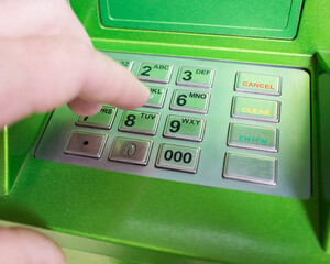 man's hand presses the buttons on the PIN keyboard of the ATM