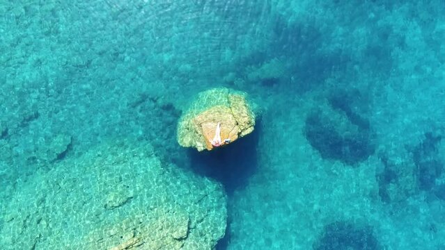 Frau auf einem Felsen in mitten eines wundersch&ouml;nen t&uuml;rkis blauen Meeres