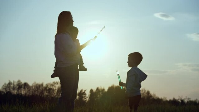 Family blowing soap bubbles at sunset. Happy smiling children and mother together. Happy childhood. High quality 4k footage